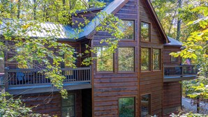 Une cabane en bois dotée d’un balcon et de grandes fenêtres, entourée d’arbres.