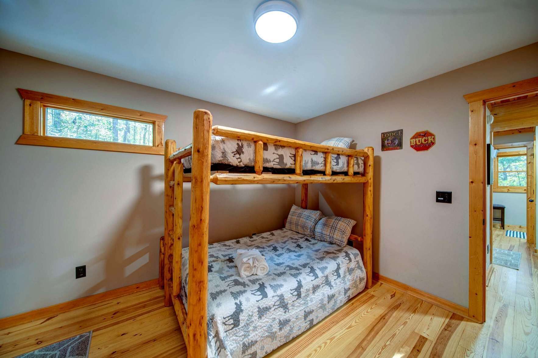 A bunk bed room with a window, wooden flooring, and a ceiling light.