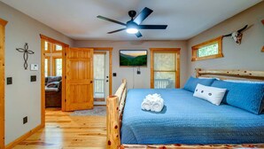 Une chambre à coucher avec un lit, un ventilateur de plafond, des murs en bois et une fenêtre avec des stores.