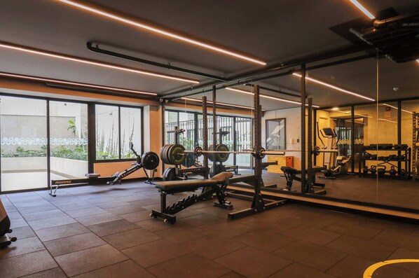 A gym with weightlifting equipment, large windows, and a mirrored wall. - w* | Amazing Loft w/ Balcony in Miraflores (Miraflores)