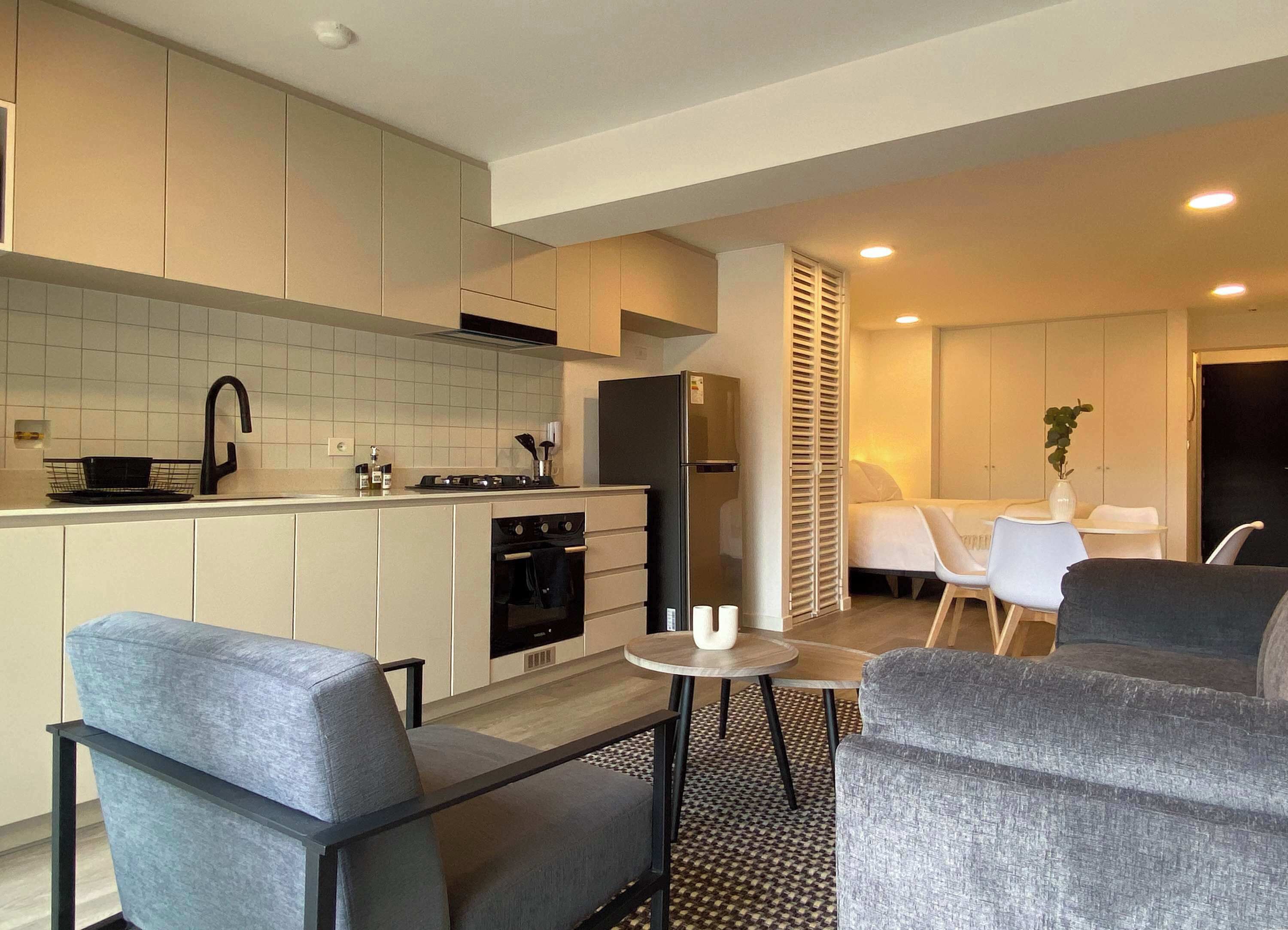 A modern kitchen with white cabinets, a black refrigerator, and a stove. There is a dining area with a small table and two chairs.