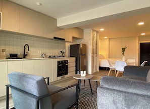 A modern kitchen with white cabinets, a black refrigerator, and a stove. There is a dining area with a small table and two chairs. - w* | Enchanting Loft w/ Balcony in Barranco (Barranco)
