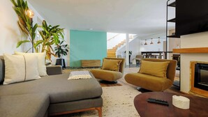 A modern living room with a grey sofa, two armchairs, a coffee table, and a fireplace. There are potted plants and a staircase leading to another level. - w* | Amazing 4BR w/ Terrace in Juarez (Ciudad de México)
