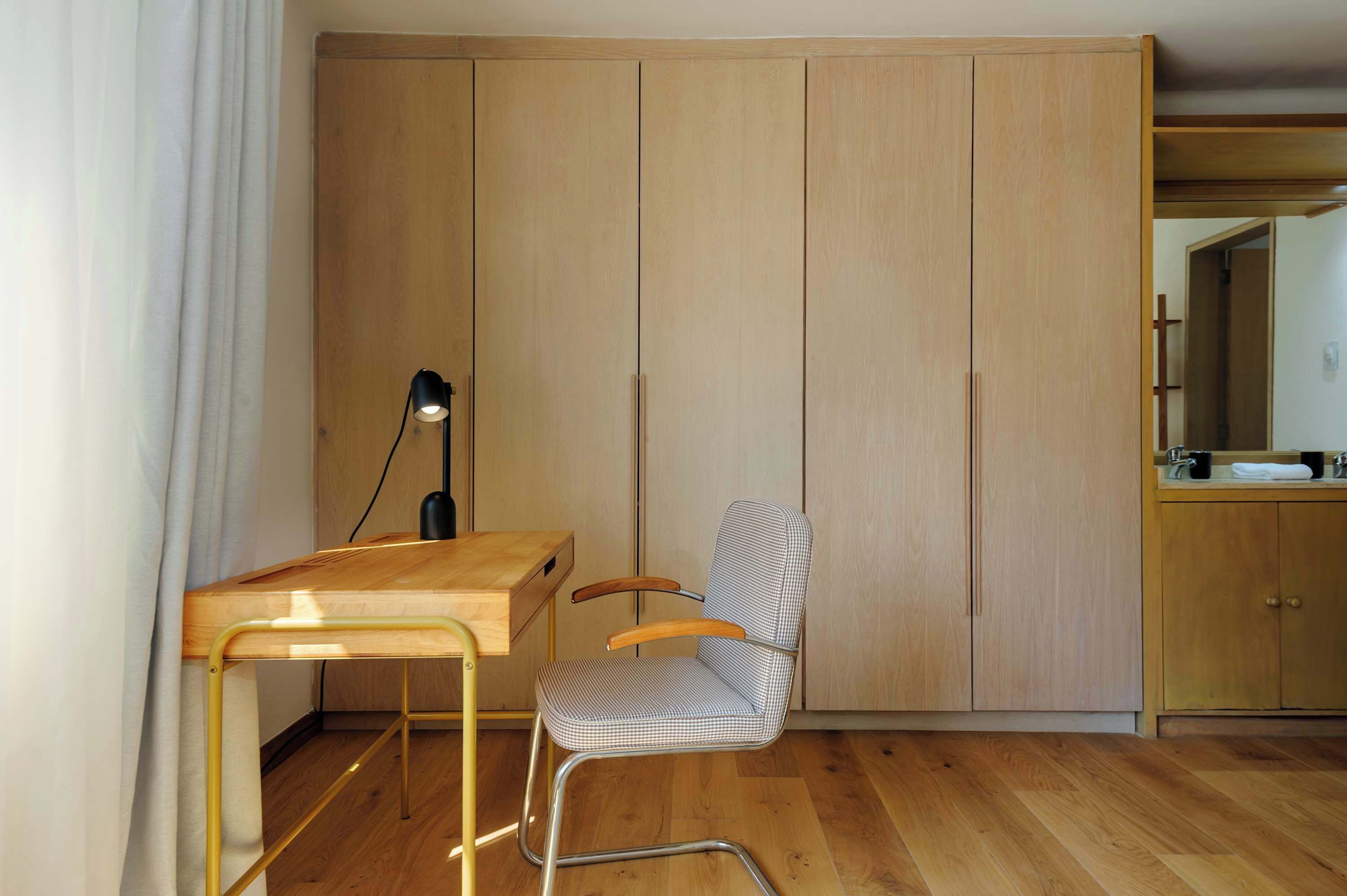 Une petite pièce avec un bureau en bois, une chaise, une armoire et un miroir.