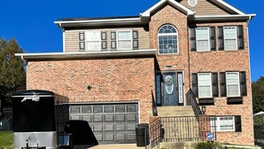 A two-story brick house with a garage, a front porch, and a small driveway. - Cozy Apartment in Superb Fort Washington MD-Private Keyless Entry. (Fort Washington)