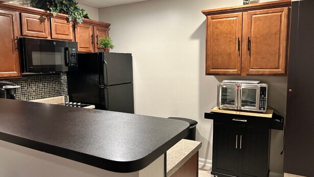A kitchen with wooden cabinets, a black refrigerator, a microwave, a toaster, and a small countertop. - Cozy Apartment in Superb Fort Washington MD-Private Keyless Entry. (Fort Washington)