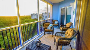 A balcony with wicker furniture, a view of buildings, and a blue wall. - Oceanwalk Getaway w/Heated Pool + Rocket Views (New Smyrna Beach)