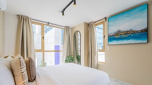 Une chambre à coucher avec un lit, des rideaux, un tableau et une fenêtre donnant sur la ville.