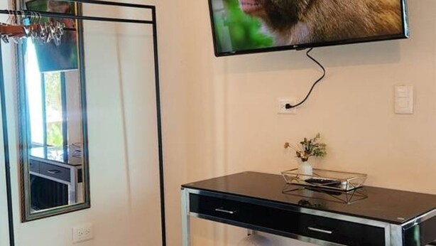 Ein Zimmer mit an der Wand befestigtem Fernseher, einem Schreibtisch mit Mülleimer und einem Spiegel.
