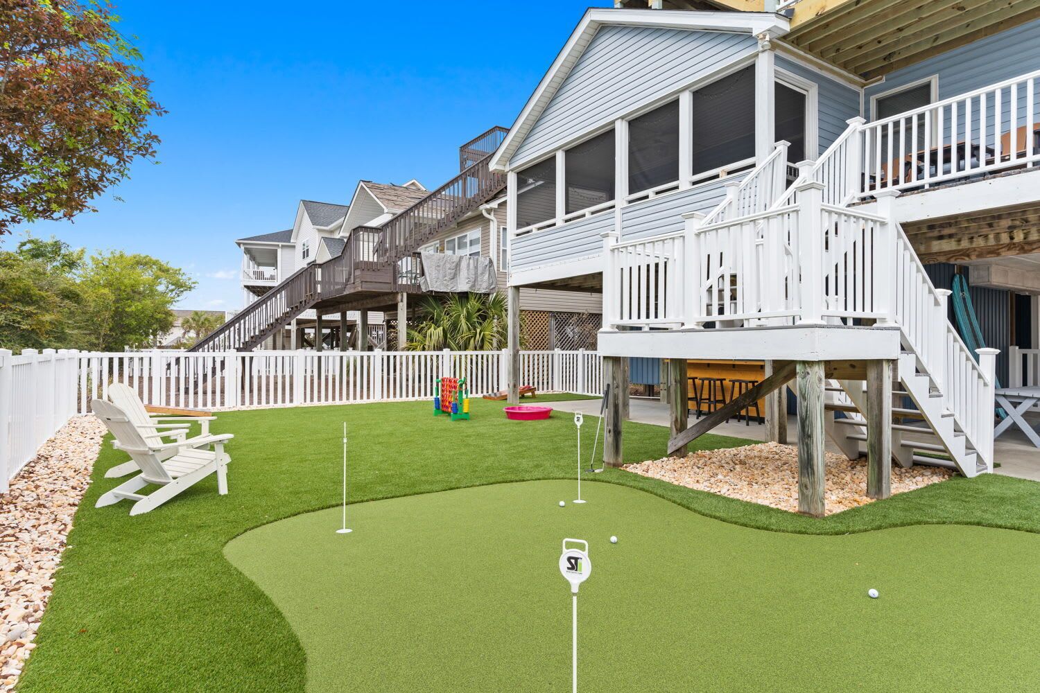 A residential property with a backyard featuring a putting green, a wooden deck, and a white fence.