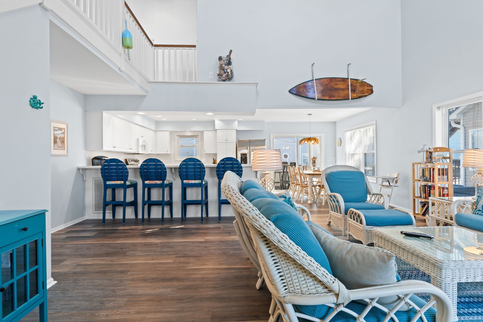 A spacious living area with a high ceiling, a kitchen in the background, and a dining area with blue chairs.