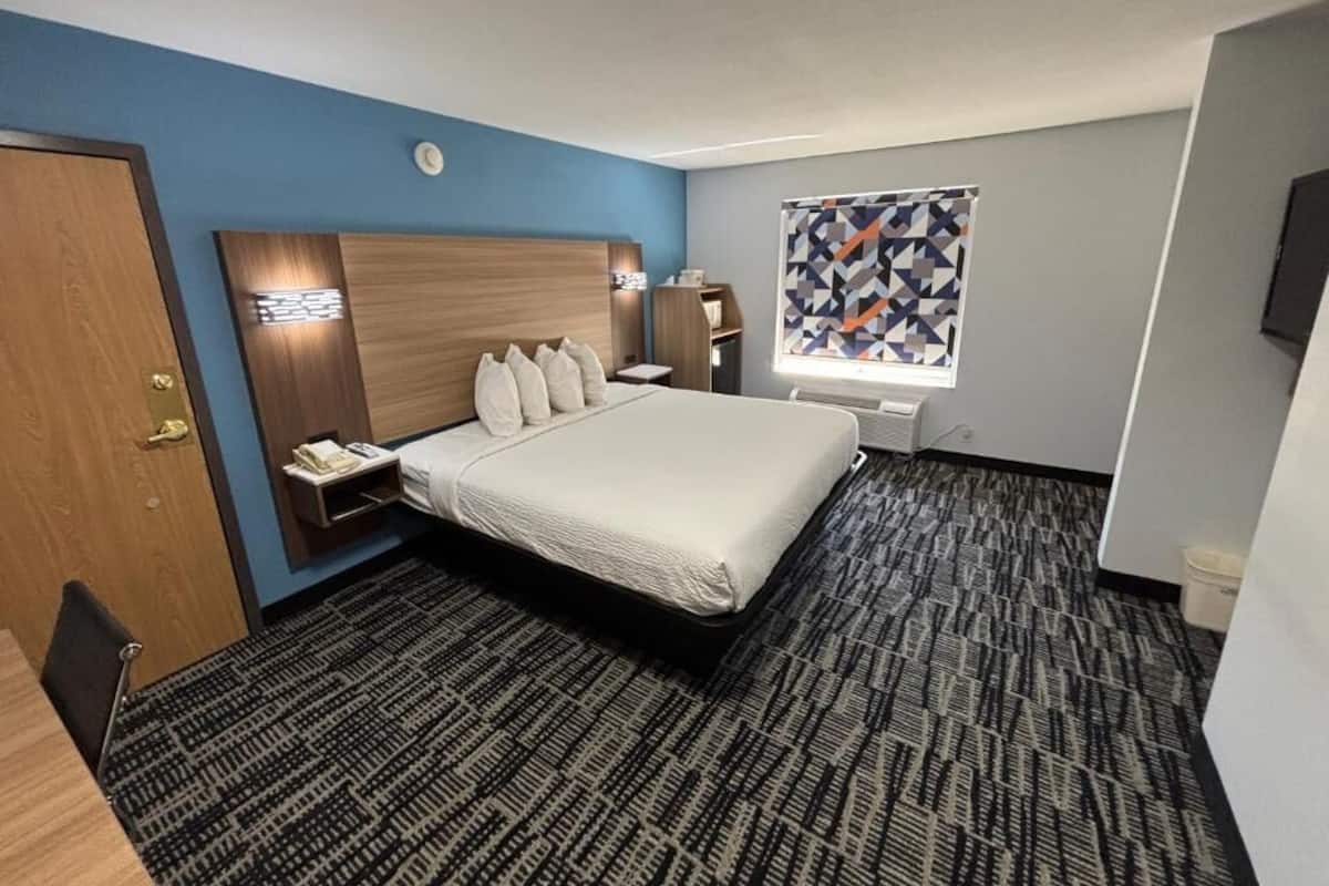 Hotelkamer met een groot bed, nachtkastje, raam met een geometrisch patroon gordijn en een vloerbedekking.