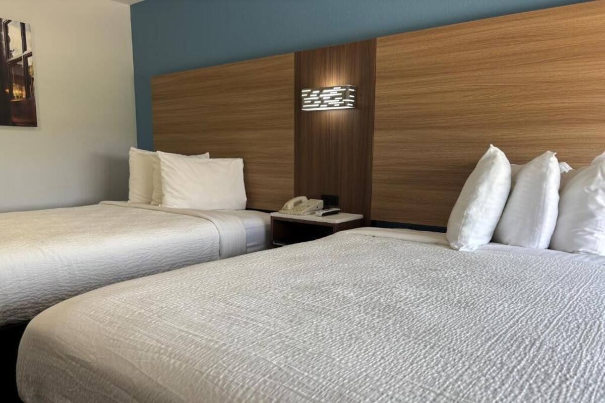 Een hotelkamer met twee bedden, een houten hoofdbord, een nachtkastje met een telefoon en een wandlamp.