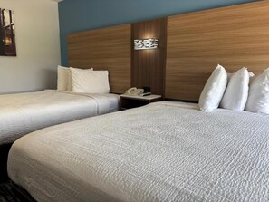 Una camera d'albergo con due letti, una testata del letto in legno, un comodino con il telefono e una lampada a parete.