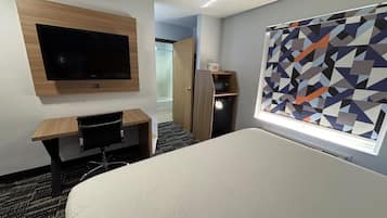 A hotel room with a bed, a desk, a television mounted on the wall, and a window with a geometric pattern.