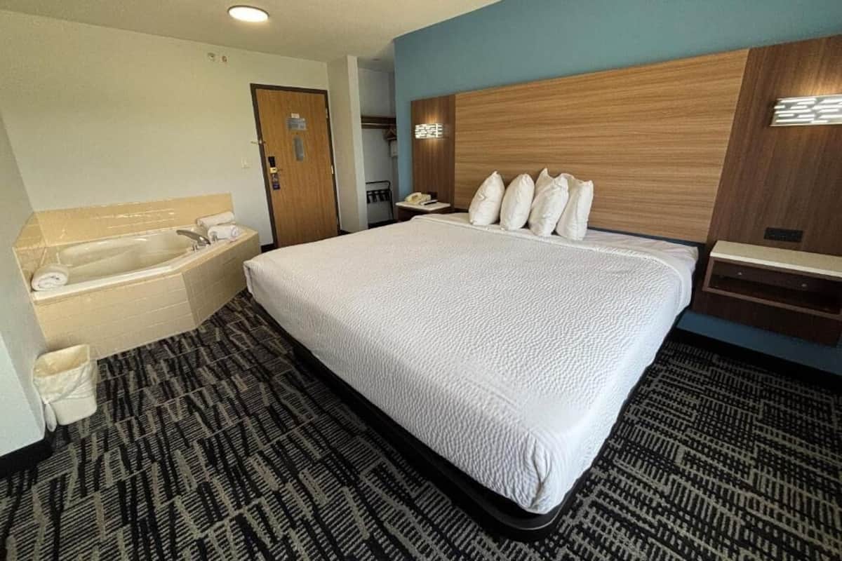 Een hotelkamer met een groot bed, een aparte badkamer met een badkuip en een houten hoofdeinde.