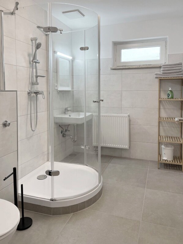 Un baño moderno con ducha envuelta en vidrio, un lavamanos y un inodoro.