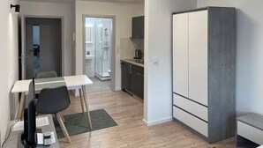 Un espacio habitable moderno y compacto con kitchenette, comedor y ducha.