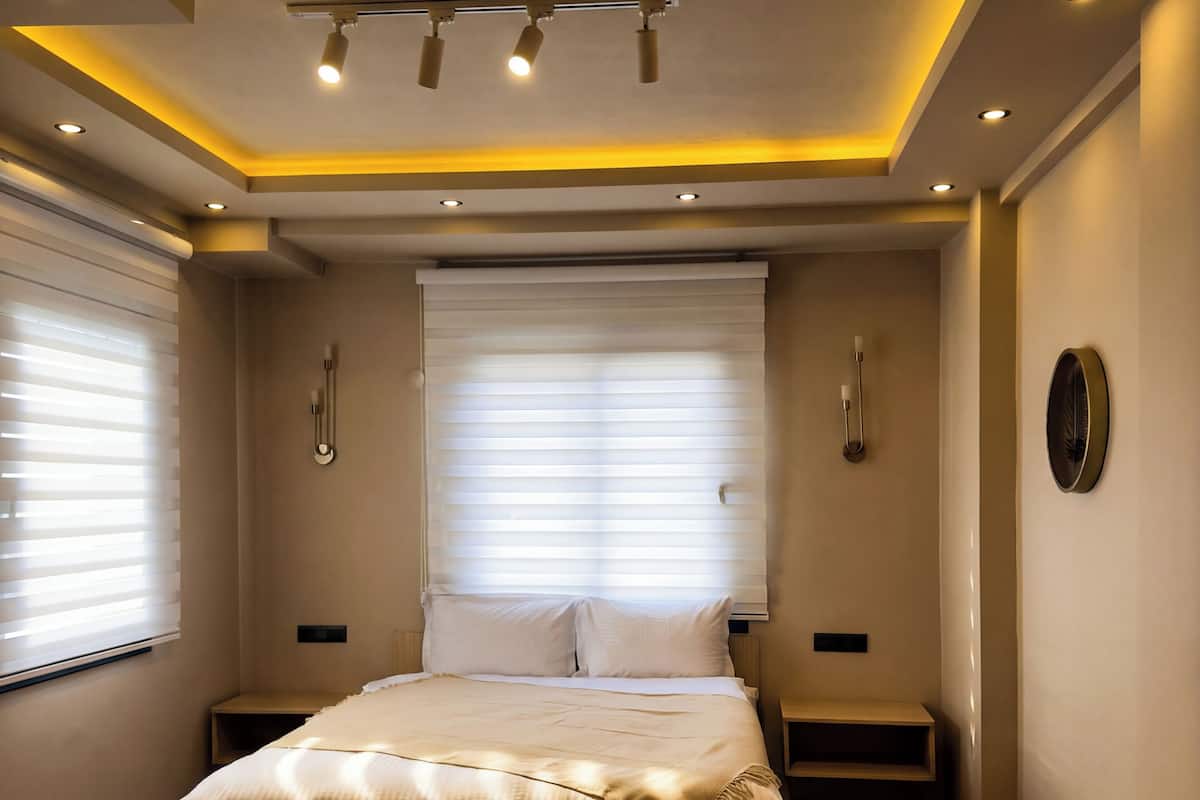 A modern bedroom with a large bed, bedside tables, a bedside lamp, and a window with blinds.