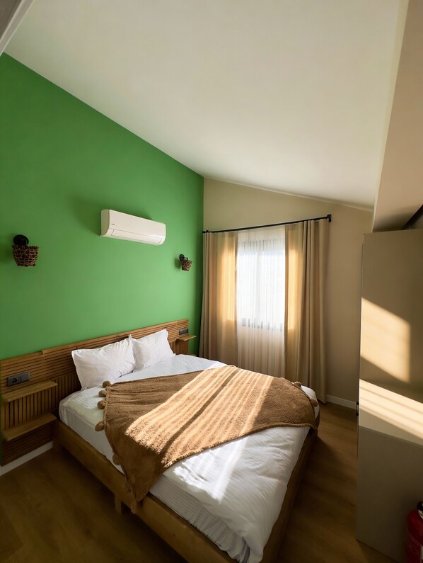 A room with a green wall, a wooden bed with white bedding, a brown blanket, and a window with curtains.
