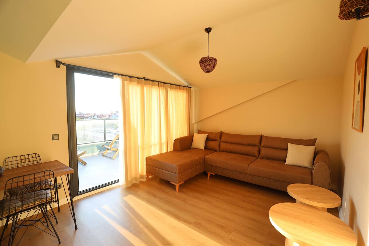 A living room with a sectional sofa, a dining table with chairs, and a small round table.
