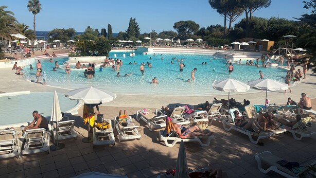 Un área de piscina con varias piscinas, tumbonas y sombrillas.