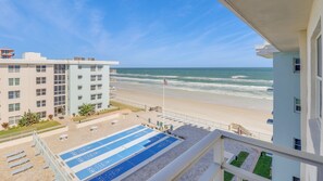A view of a beach from a balcony with a pool table and lounge chairs.