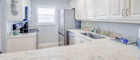 Una cocina moderna con armarios blancos, un refrigerador de acero inoxidable, un lavamanos doble y una encimera de granito.