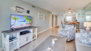 A living room with a flat-screen TV, a white entertainment unit, a gray sofa with star patterns, and a dining area with a wooden table and chairs. - Pet-Friendly Paradise @ Sea Coast Gardens (New Smyrna Beach)