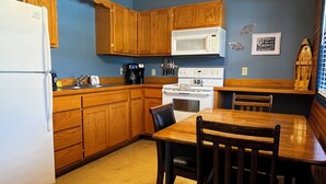 A compact kitchen with wooden cabinets, a white refrigerator, a microwave, and a dining table with chairs. - Stay in cozy cabin 5 off of Lake of the Ozarks in beautiful Sunrise Beach, MO (Sunrise Beach)