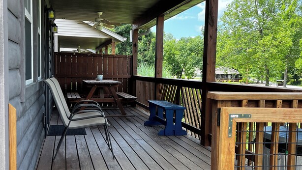 A wooden deck with a covered area, outdoor furniture, and a view of a residential neighborhood. - Stay in cozy cabin 5 off of Lake of the Ozarks in beautiful Sunrise Beach, MO (Sunrise Beach)
