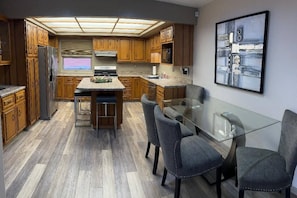 A modern kitchen with wooden cabinets, a central island, and a glass dining table with chairs. - Perfect Black Hills Getaway (Rapid City)