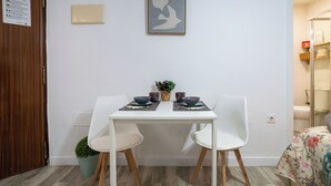Een eetgedeelte met een witte tafel, twee stoelen en een lijst met kunstwerk aan de muur.