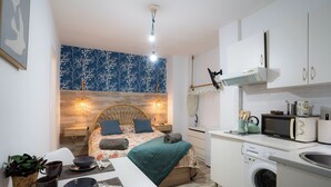 Een compacte slaapkamer met een bed, nachtkastje en een kleine kitchenette met een magnetron en wasmachine.