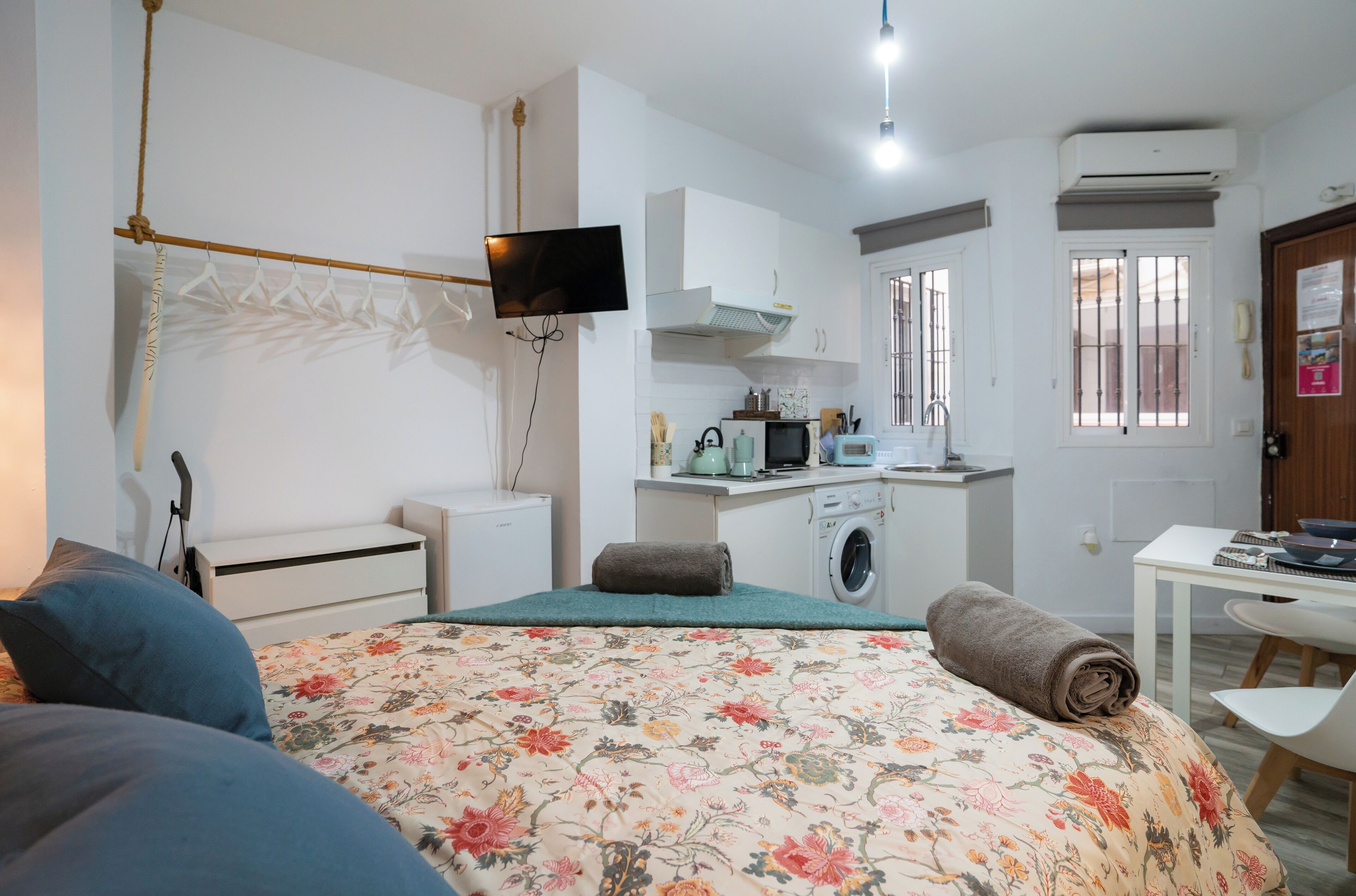 Une chambre avec un lit, un bureau, un lave-linge et un téléviseur fixé au mur.