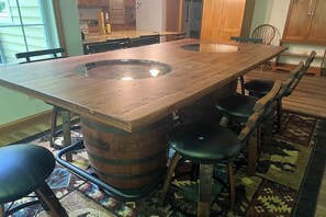 Un espace repas avec une grande table en bois, des tabourets de bar et une cuisine en arrière-plan.