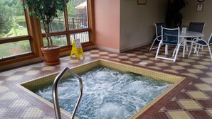 A hot tub with a metal ladder, surrounded by checkered floor tiles and a window with a view of greenery. -  House in Lincoln, NH 2 Miles to Loon with Forest Ridge sports club access (Lincoln)