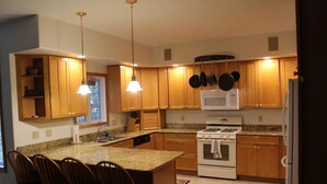 A kitchen with wooden cabinets, a granite countertop, a built-in oven, and a microwave. There are bar stools and pendant lights. -  House in Lincoln, NH 2 Miles to Loon with Forest Ridge sports club access (Lincoln)