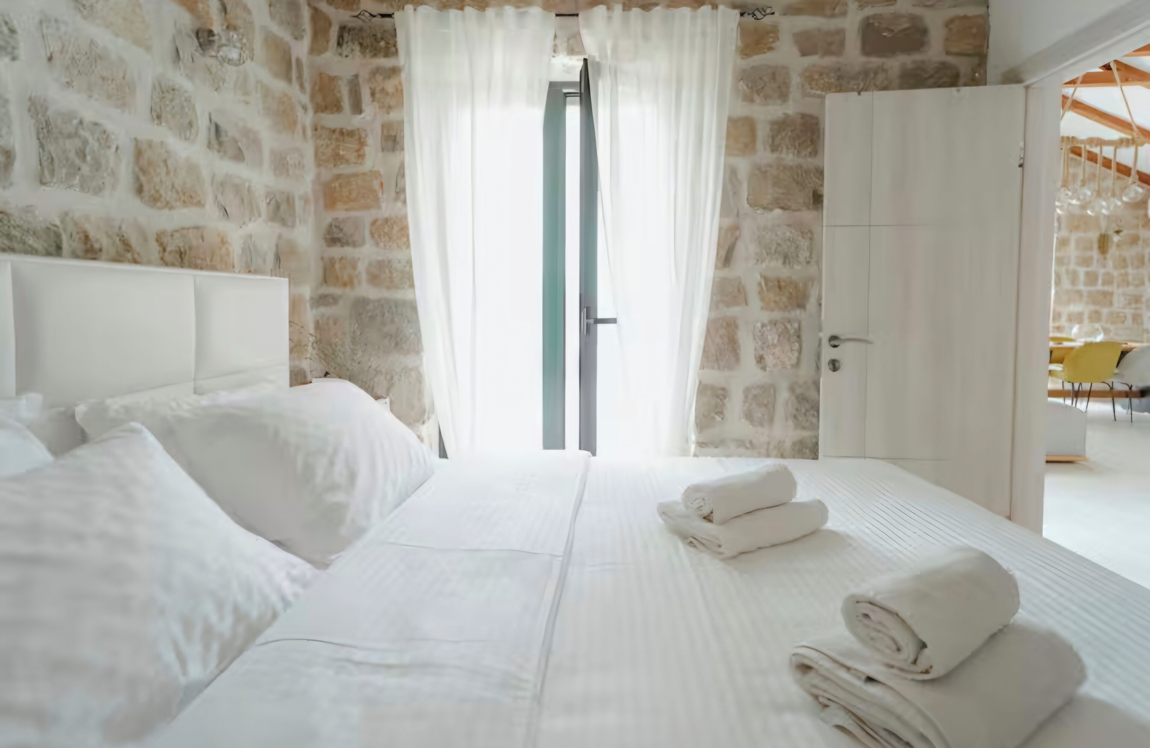 Un dormitorio con pared de piedra, una cama con ropa de cama blanca y vistas a través de una puerta.