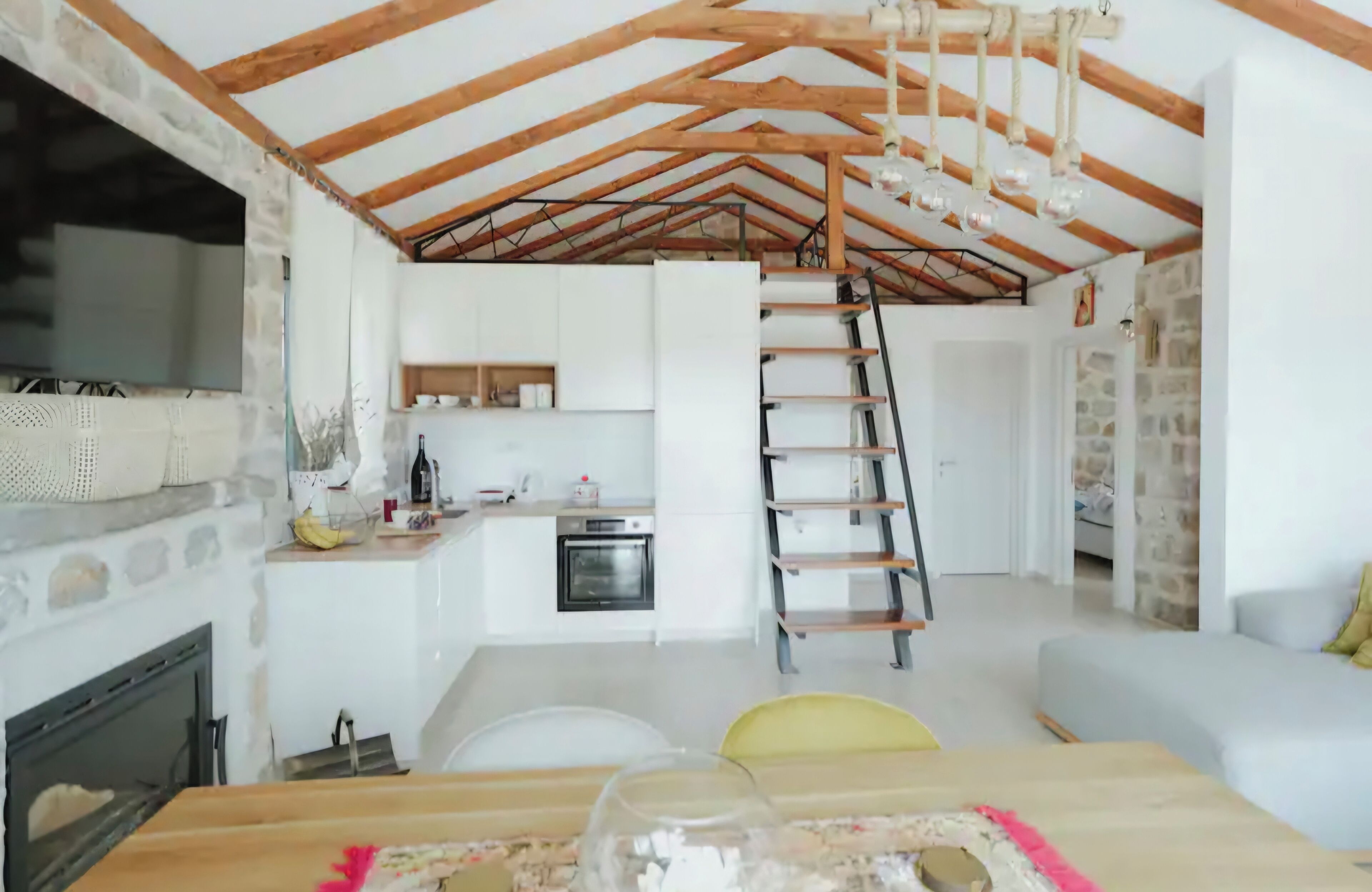 A rustic interior with exposed wooden beams, a kitchen area, a staircase, and a living space with a sofa.