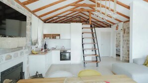 Un intérieur rustique avec des poutres apparentes, un coin cuisine, un escalier et un espace de vie doté d’un canapé.