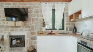 Une cuisine moderne avec un mur en pierre, une cheminée, un téléviseur à écran plat et une fenêtre ornée de rideaux légers.