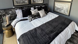 Una camera da letto moderna con un letto grande, una testiera con un murale raffigurante un panorama urbano e tre fotografie in bianco e nero di un paesaggio cittadino appese al muro.