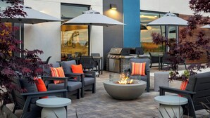 An outdoor seating area with a fire pit, outdoor grill, and umbrellas. - Towneplace Suites By Marriott Victoria Airport Sidney (Sidney)