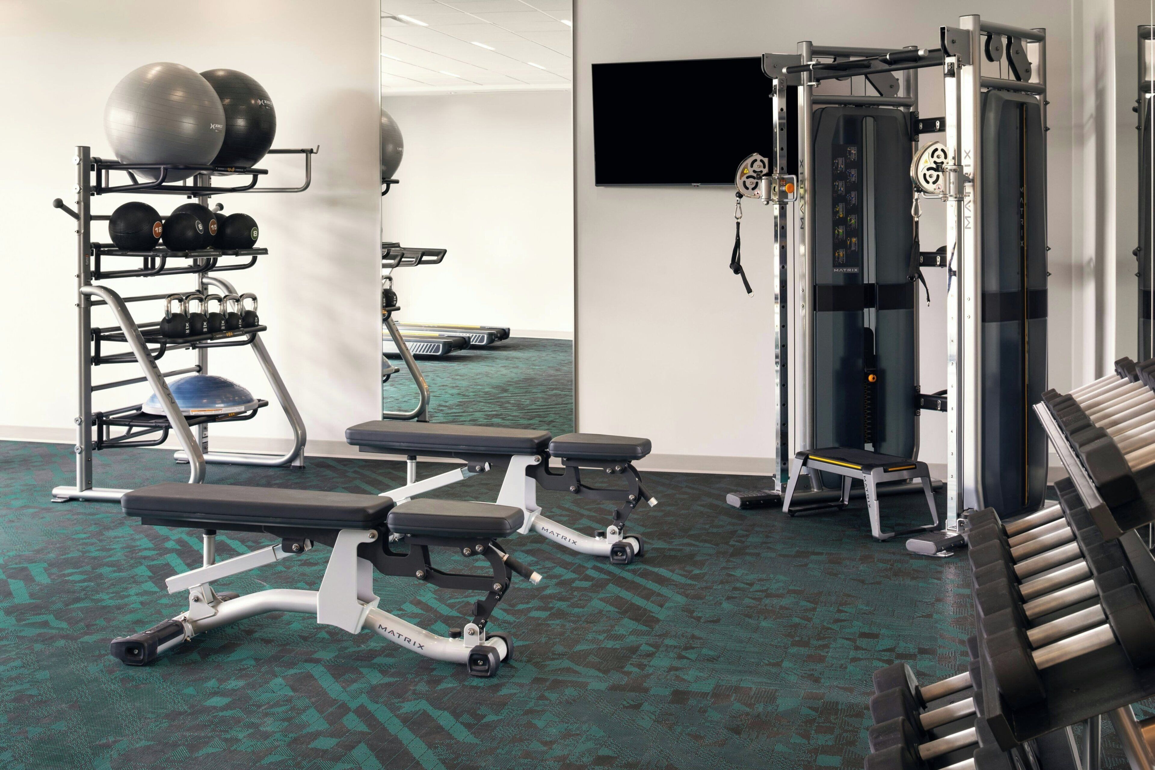 Un gimnasio con equipo de ejercicio, una banca y un televisor instalado en la pared.