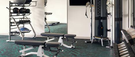 A gym with exercise equipment, a bench, and a wall-mounted TV.