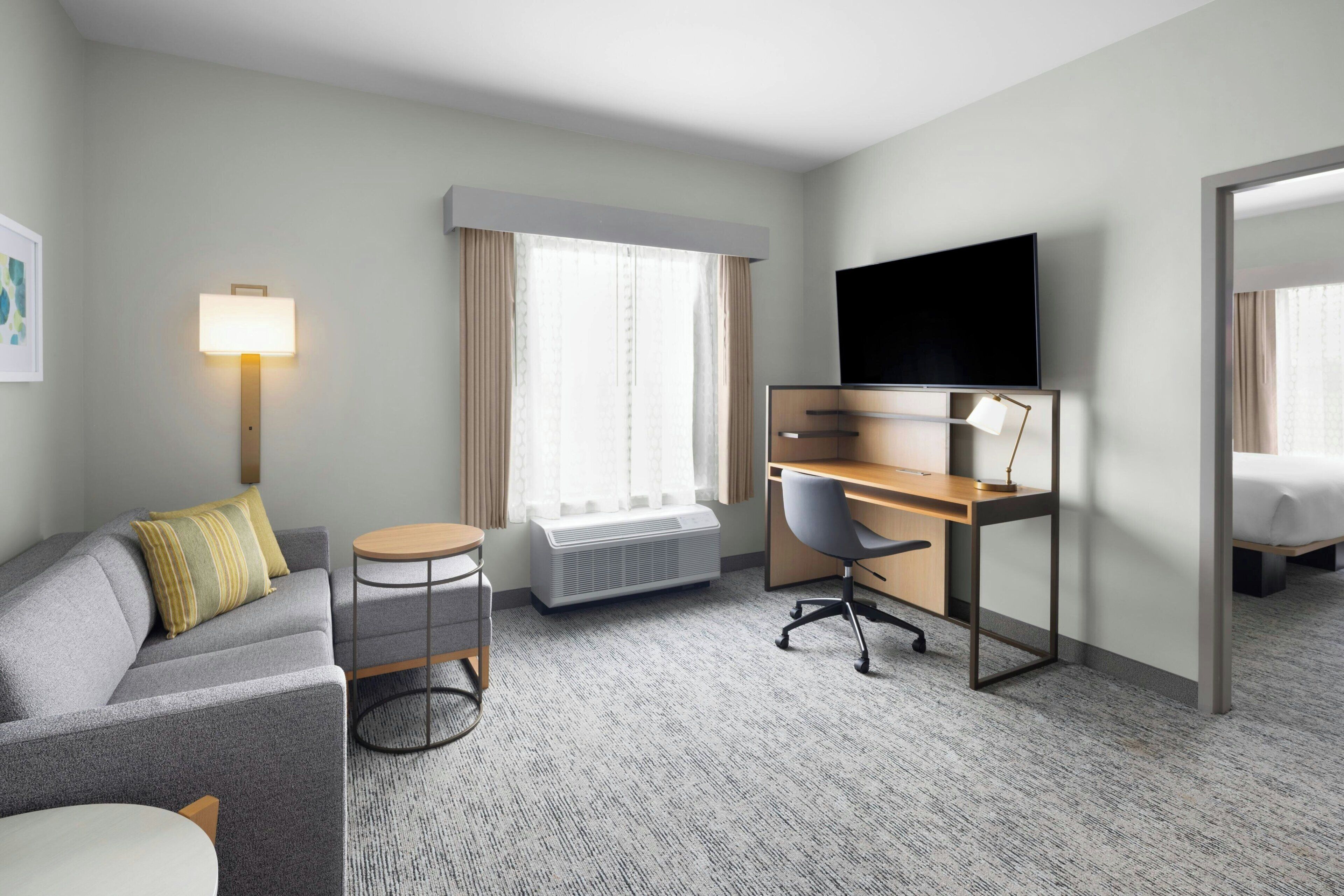 Une chambre d’hôtel équipée d’un canapé, d’un bureau avec une chaise, d’une télévision, d’un radiateur et d’une fenêtre avec des rideaux.