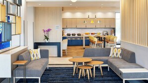 A modern hotel lobby with a seating area, a kitchen in the background, and a decorative plant. - Towneplace Suites By Marriott Victoria Airport Sidney (Sidney)