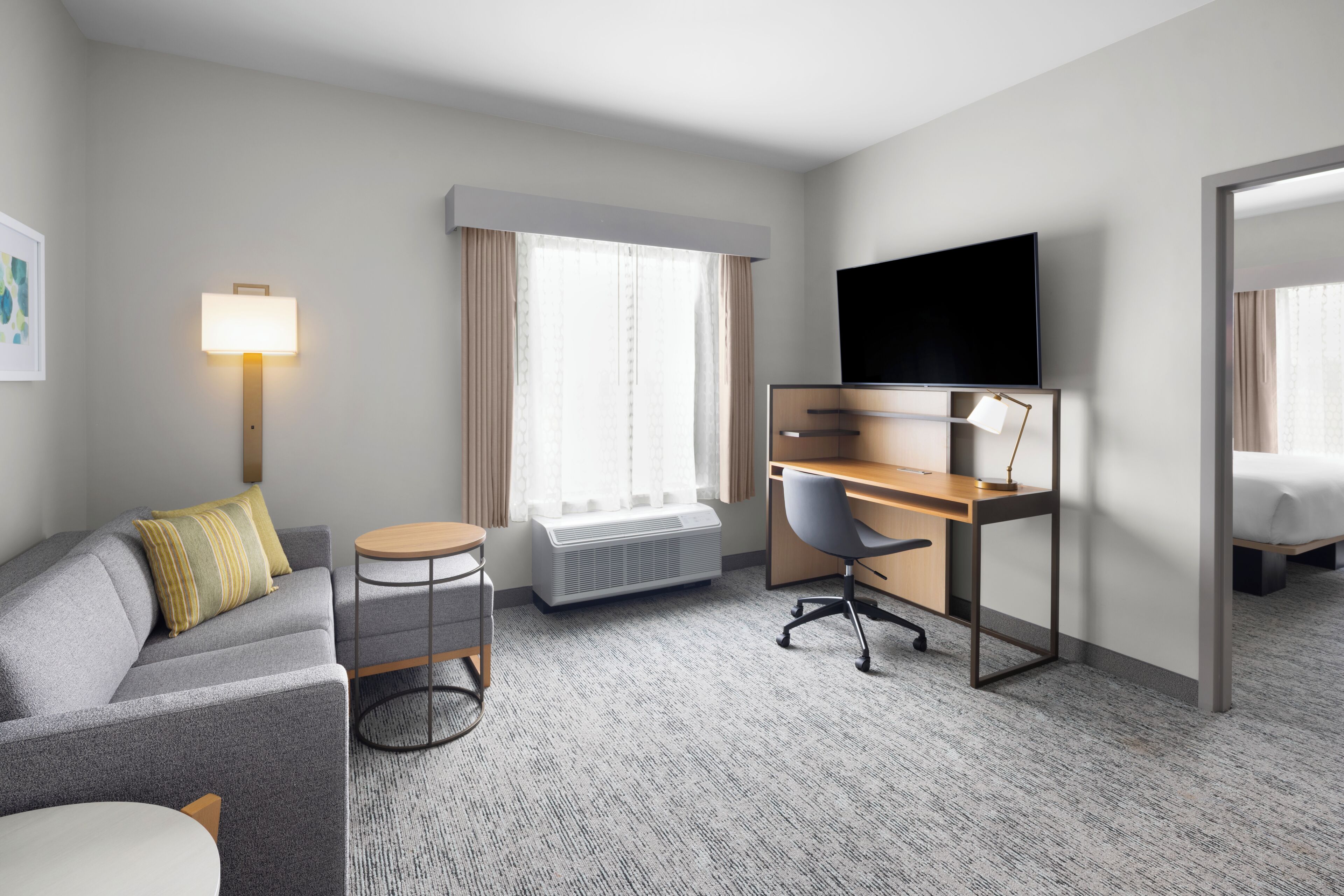 A hotel room with a sofa, desk, chair, TV, and a bed.