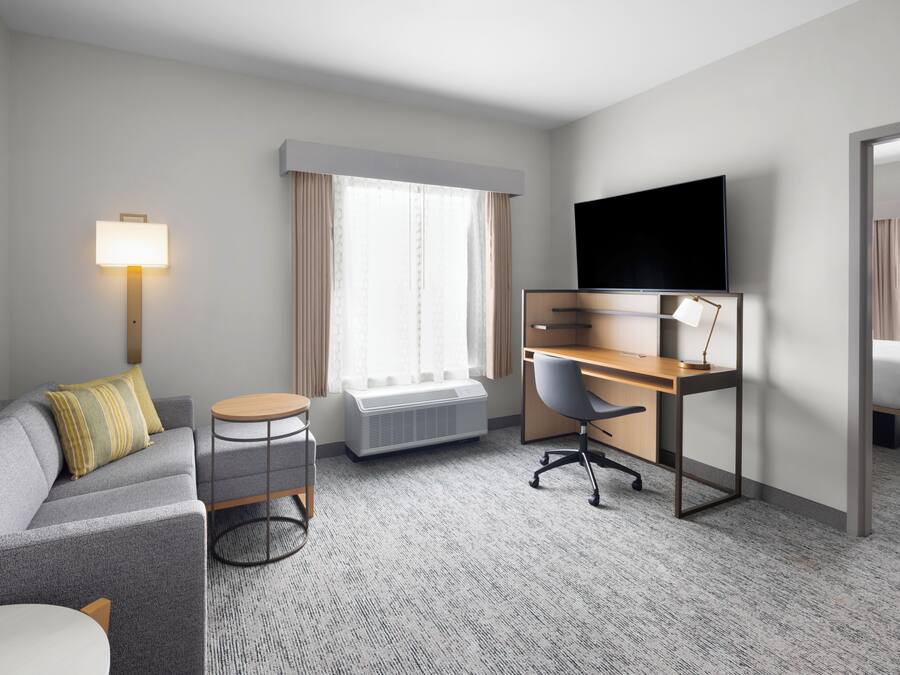 A hotel room with a sofa, desk, chair, TV, and a bed.